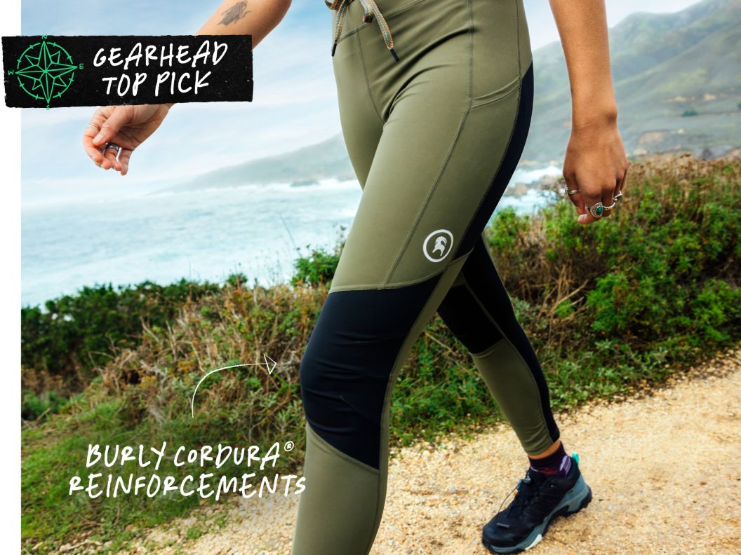 A closeup of leggings as a woman walks down a trail near the ocean. Text overlay reads: gearhead top pick, burly cordura reinforcements.